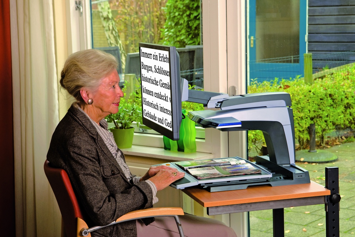 Eine ältere Dame sitzt vor einem Bildschirmlesegerät.