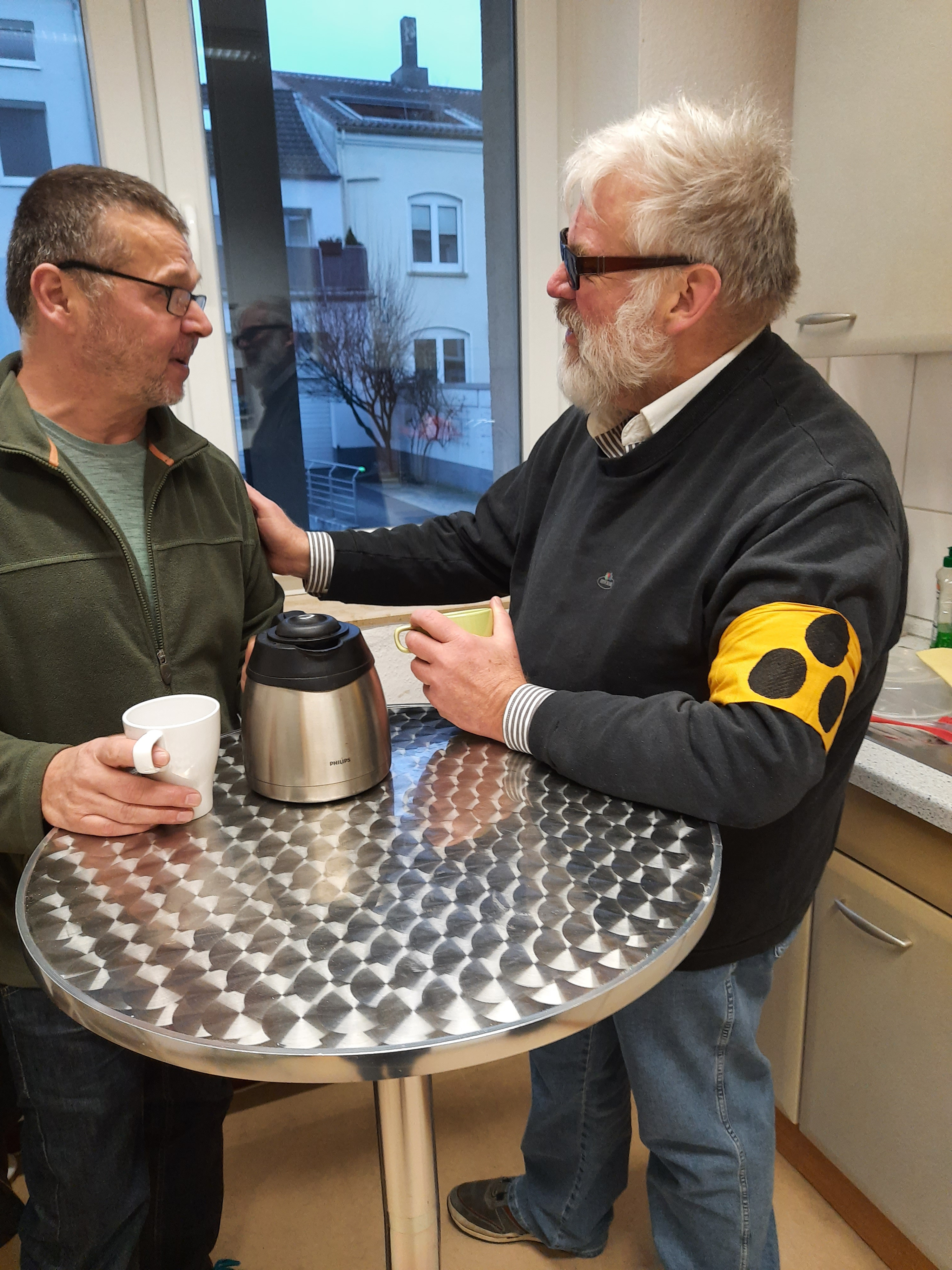 Ein sehender Helfer und ein blinder Mann lachen und trinken Kaffee zusammen